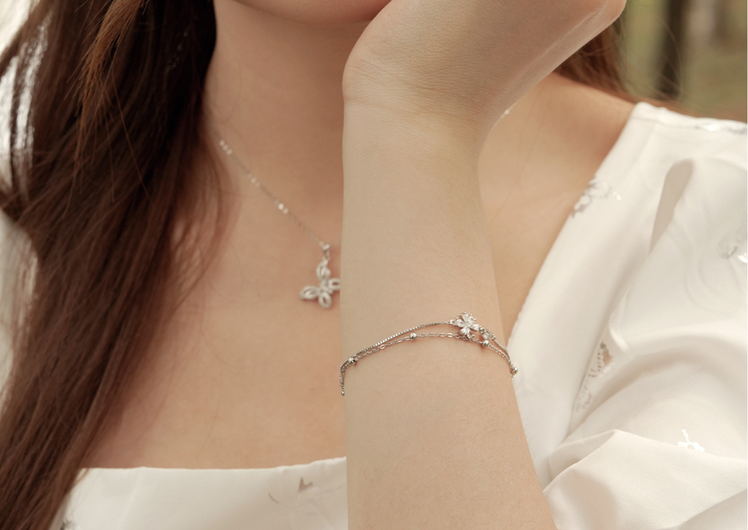 Model memakai gelang DAVINA Florae warna silver dengan desain bunga yang elegan, dipadukan dengan dress putih dan kalung senada.
