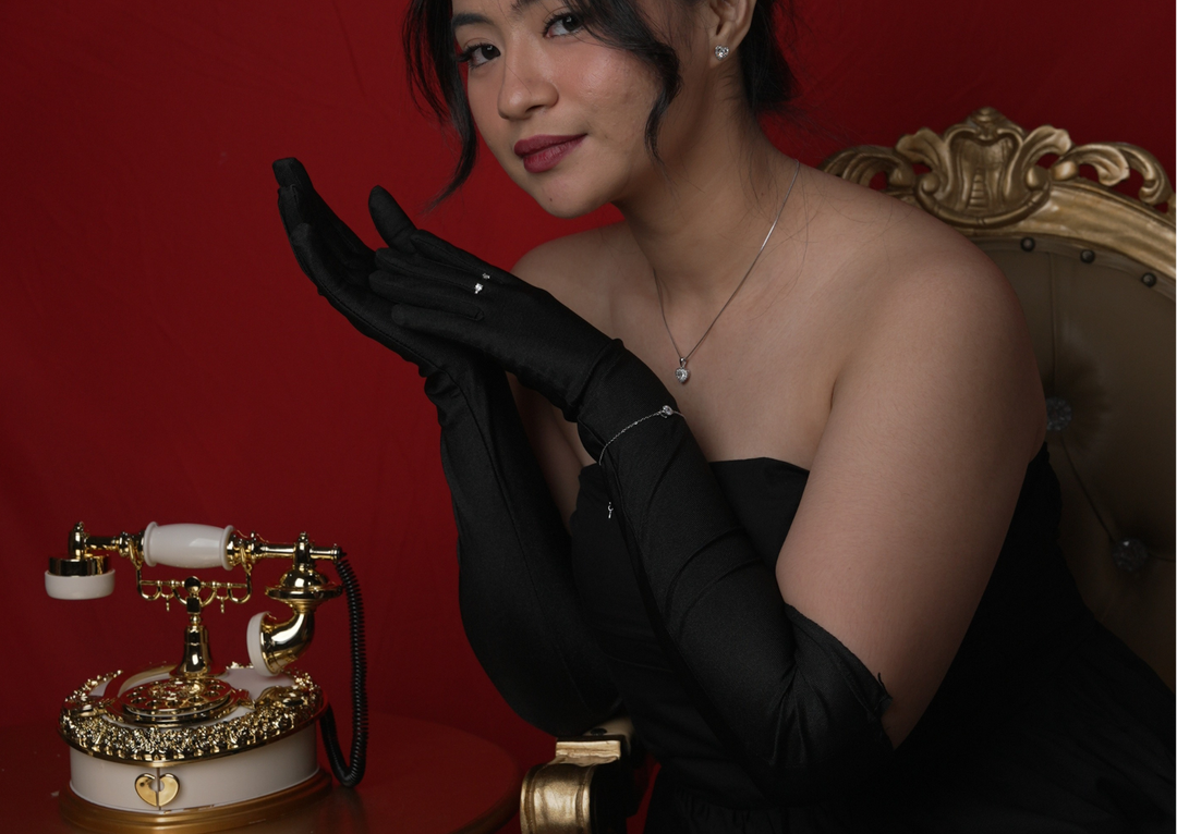 Seorang wanita memakai set perhiasan silver DAVINA (kalung hati, gelang, cincin, anting), foto editorial bernuansa klasik dengan telepon jadul.