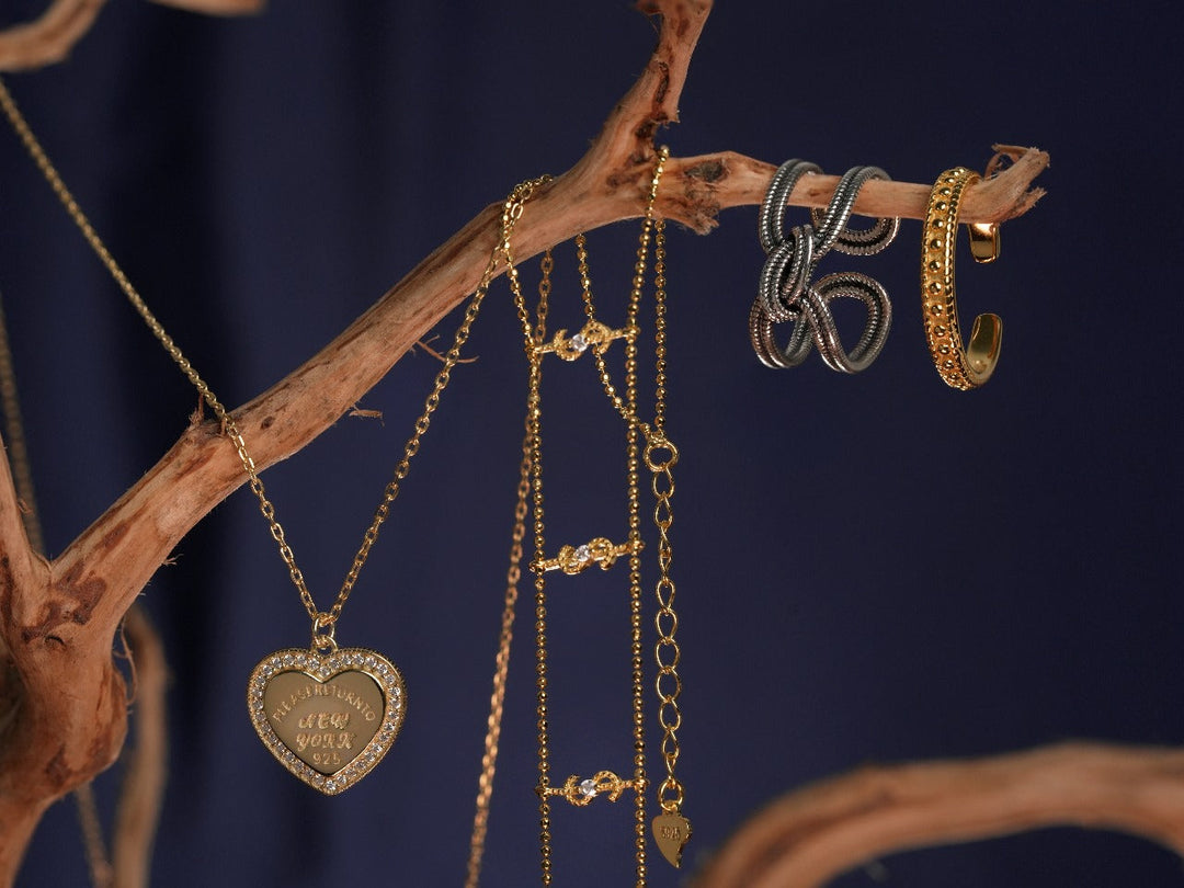 Deretan perhiasan vintage DAVINA yang digantung pada ranting kayu, terdiri dari kalung liontin hati, gelang rantai emas, cincin twist silver, dan cincin bertekstur gold. Ditampilkan dengan latar biru gelap yang memberi kesan hangat, klasik, dan elegan.